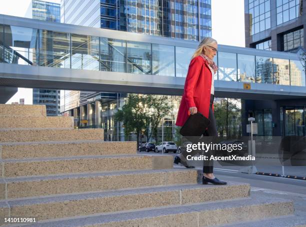 senior female business executive ascends concrete staircase, business district behind - calgary bridge stock pictures, royalty-free photos & images