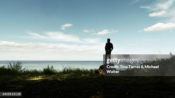 a man stands by the sea and enjoys the view. rear view. backlight. - cliff stock pictures, royalty-free photos & images