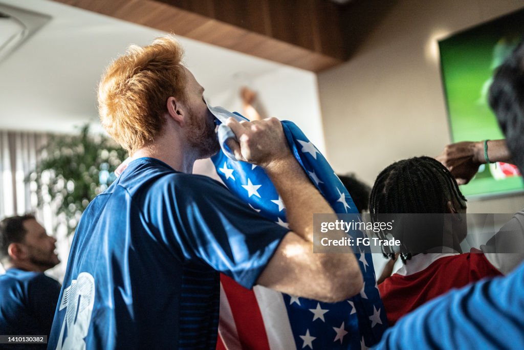 Sports fan celebrating holding american flag at home