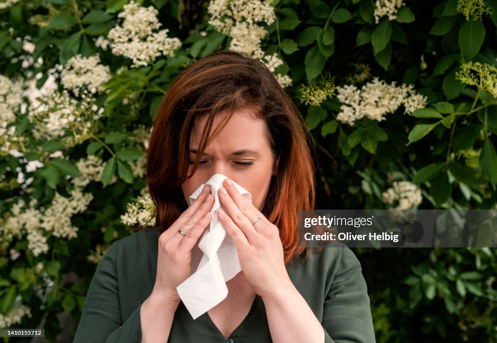 A redhead woman suffers from hay fever and sneezes into a handkerchief
