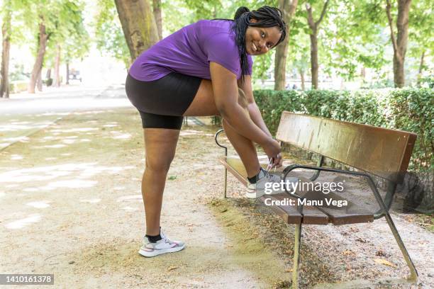 a young woman tying up shoelaces getting ready to start her exercises in the park - fat legs stock pictures, royalty-free photos & images