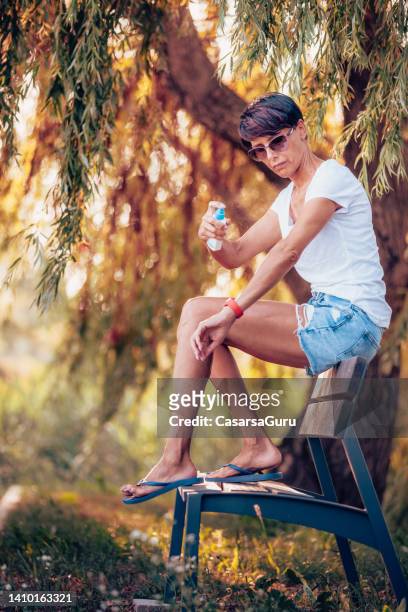 woman spraying mosquito repellent on her arms - insect repellent stock pictures, royalty-free photos & images