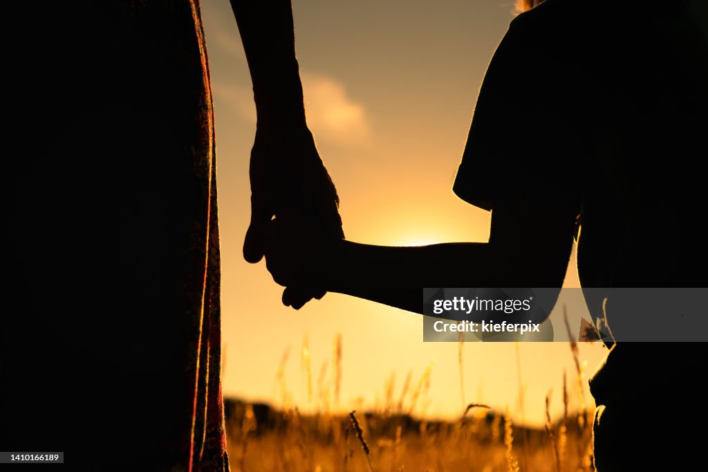Silhouette of mother and child holding hands facing the sunset.