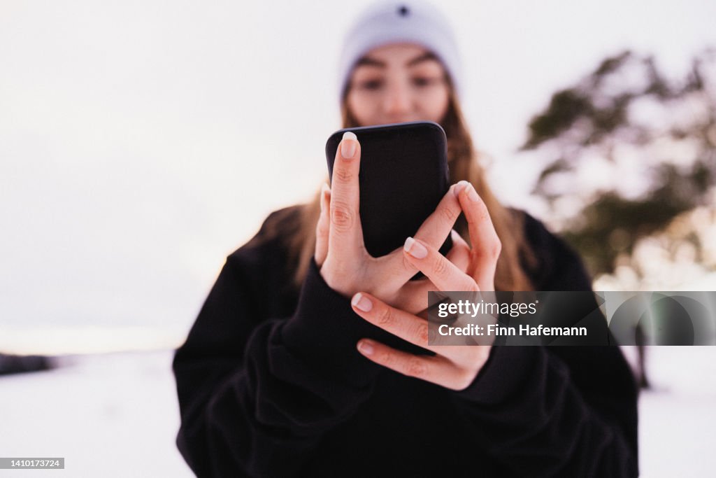 Teenage Girl Reading Good News On Mobile Phone Outdoors In Winter