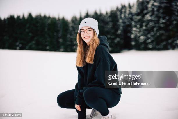 happy smiling teenage girl sitting in the snow winter landscape of black forest germany - girls in leggings stock-fotos und bilder