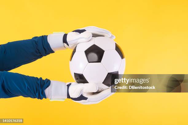 detail the arms and hands of a soccer goalkeeper in a teal shirt and white gloves, catching a ball, on a yellow background. soccer, sport, competition, world cup and qatar concept. - goalkeeper hand stock pictures, royalty-free photos & images