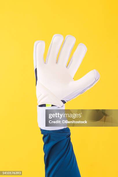 detail of the arm of a soccer goalkeeper with a greenish blue shirt and white gloves, on a yellow background. soccer, sport, competition, world cup and qatar concept. - goalkeeper hand stock pictures, royalty-free photos & images