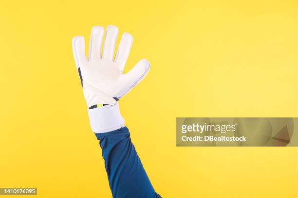 detail of the arm of a soccer goalkeeper with a greenish blue shirt and white gloves, on a yellow background. soccer, sport, competition, world cup and qatar concept. - goalkeeper gloves stock pictures, royalty-free photos & images