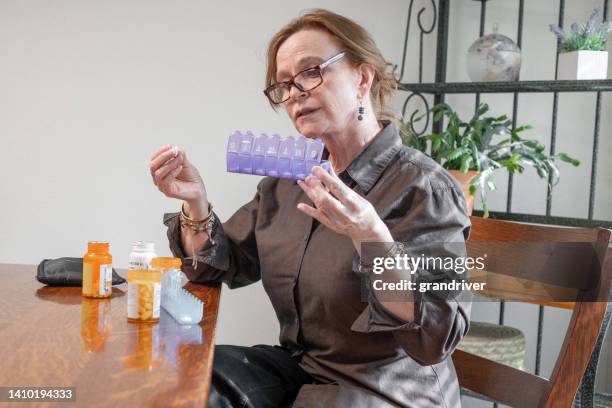 elderly woman struggling to fill her daily prescription container in a middle class home - surprised woman looking at tablet stock pictures, royalty-free photos & images