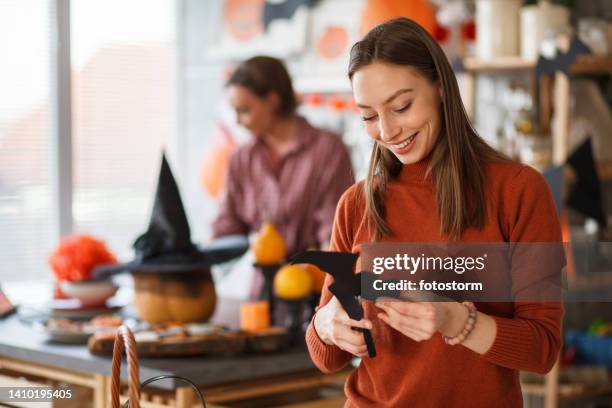 young joyful woman cutting out a paper bat when making halloween decorations - halloween craft stock pictures, royalty-free photos & images