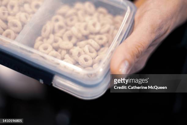 woman holds plastic container full of dry cereal for a healthy snack - cheerios stock-fotos und bilder
