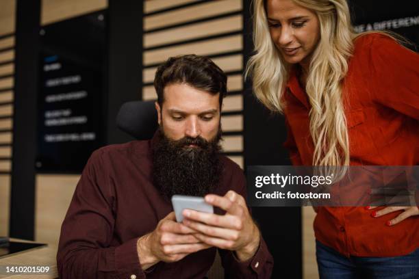 two young business colleagues looking at memes via smart phone during office break - meme stock stock pictures, royalty-free photos & images