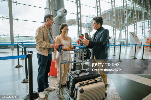 tiro de um casal de idosos idosos asiáticos alegres mostrando cartão de embarque para o assistente de passageiros na área de partida do aeroporto. - balcão de check in do aeroporto - fotografias e filmes do acervo