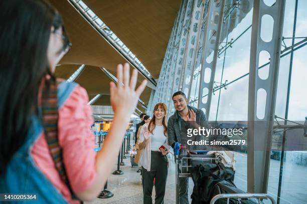willkommen zurück, mama und papa. glückliches junges asiatisches chinesisches mädchen, das mit der hand winkt und ihre mutter und ihren vater in der ankunftshalle am flughafen begrüßt, - kuala lumpur airport stock-fotos und bilder