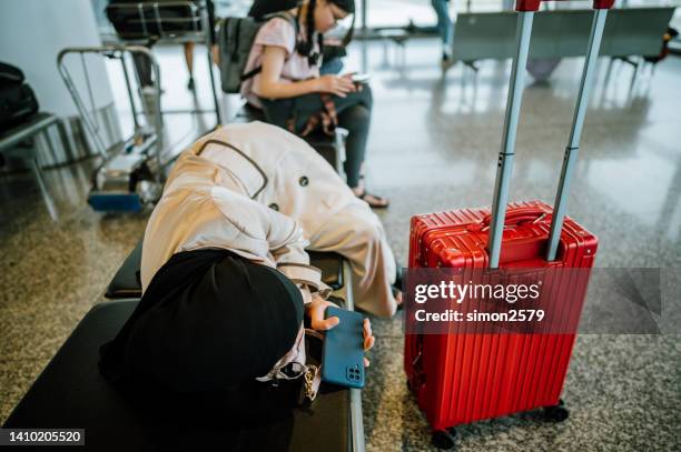 young asian business woman with hijab waiting for delayed flight and sleeping on chairs at airport - jet lag stockfoto's en -beelden
