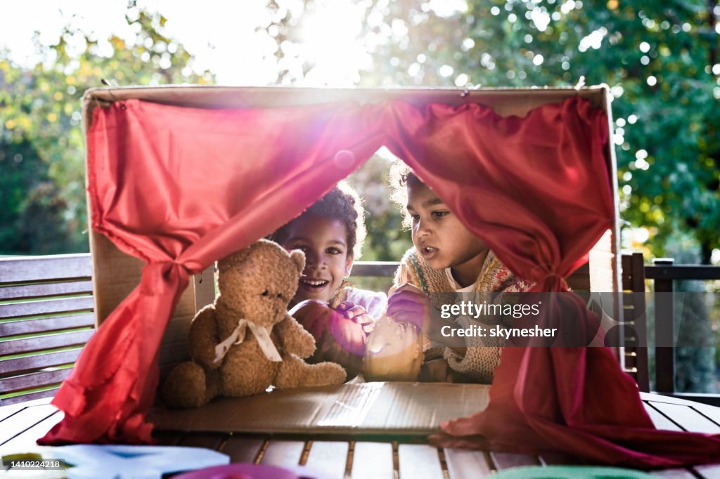 Happy black kids having a puppet show on a terrace.