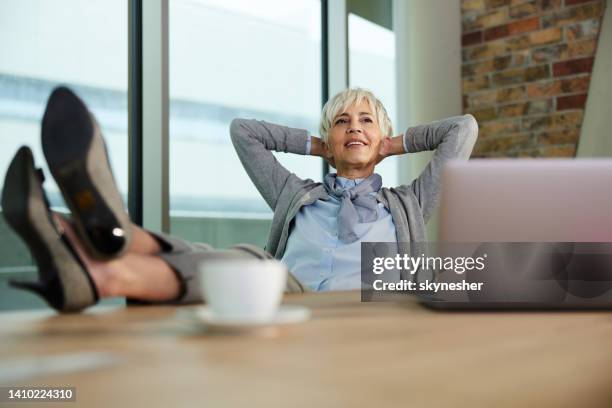 relaxed mature businesswoman taking a break in the office. - hands behind head stock pictures, royalty-free photos & images