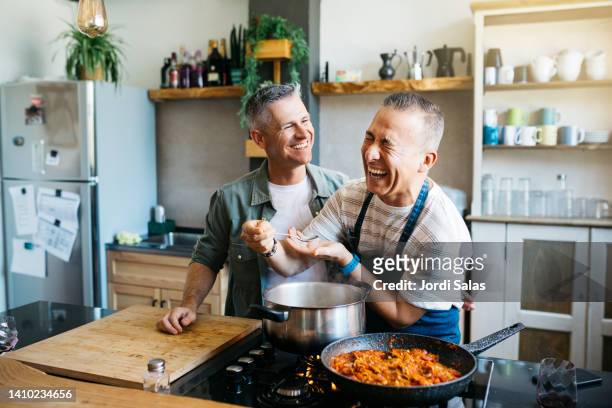 gay couple having fun while cooking - kitchen photos et images de collection