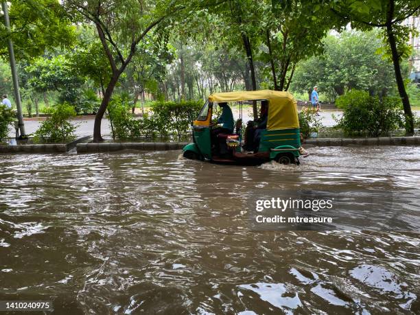 imagen de una carretera inundada con un tuk tuk de rickshaw verde y amarillo conduciendo a través de una zona residencial anegada en la temporada de monzones ghaziabad, uttar pradesh, india - uttar pradesh fotografías e imágenes de stock