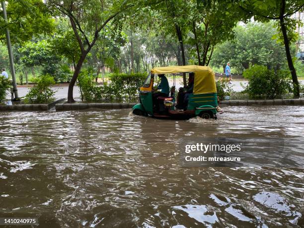 image of flooded road with green and yellow auto rickshaw tuk tuk driving through a waterlogged residential area in monsoon season ghaziabad, uttar pradesh, india - uttar pradesh stock pictures, royalty-free photos & images