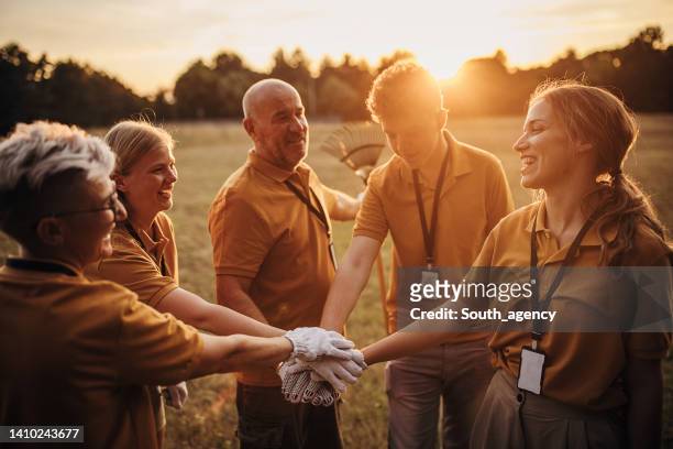 happy community service volunteers cleaning up the park gathered around stacking hands - dedication stock pictures, royalty-free photos & images