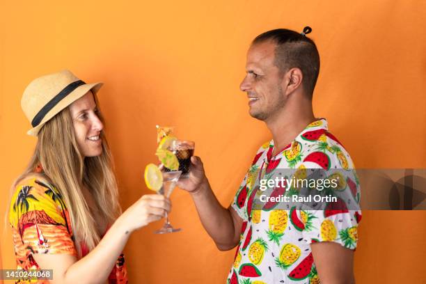 woman and man toasting with cocktails in tropical party against orange background - adult cocktail party background stock-fotos und bilder