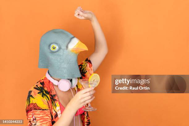 unrecognizable female wearing bird head dancing and drinking cocktail on orange background - mask party stock pictures, royalty-free photos & images