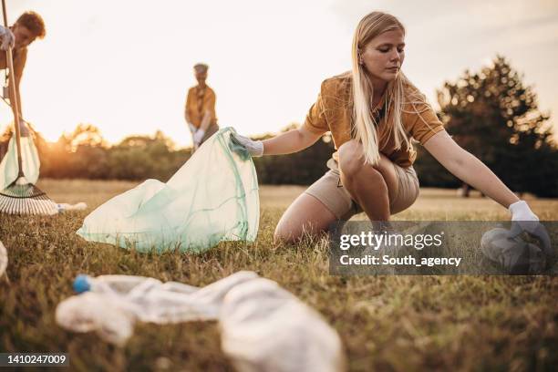 junge frau, die mit einer gruppe von freiwilligen in der natur müll aufsammelt - soziales engagement stock-fotos und bilder