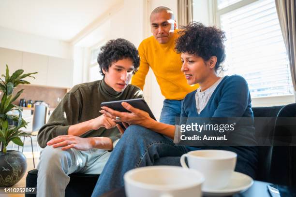 hispanic family using digital tablet together in living room - parent teen stock pictures, royalty-free photos & images
