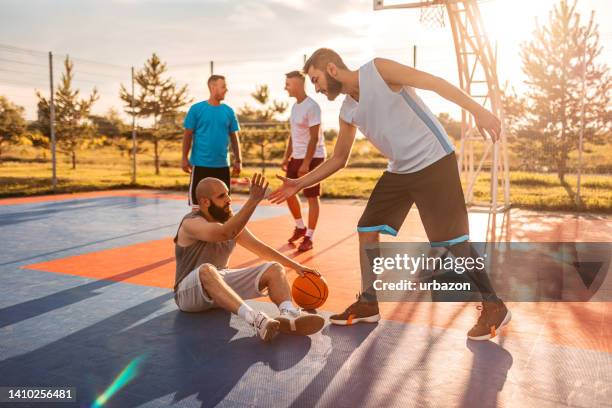 young man picking up a friend while playing a basketball game - basketball teamwork stock pictures, royalty-free photos & images