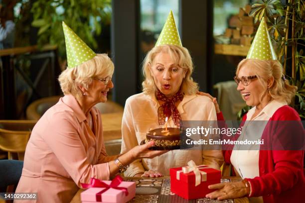 ältere dame bläst geburtstagskerze im café mit ihren freunden - oma feiert stock-fotos und bilder