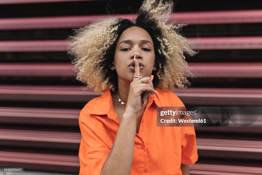 Woman making silence gesture in front of wall