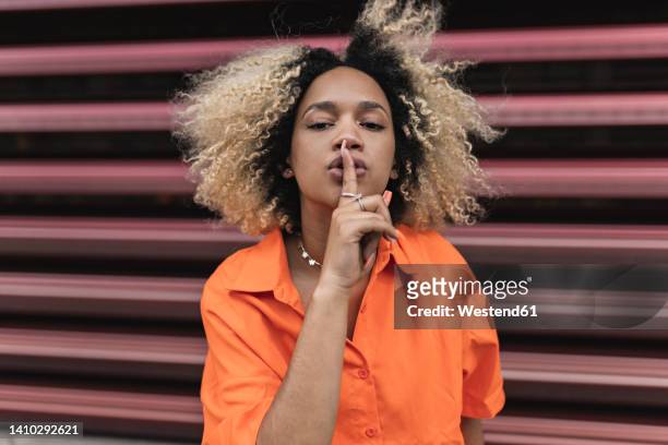 woman making silence gesture in front of wall - silêncio - fotografias e filmes do acervo
