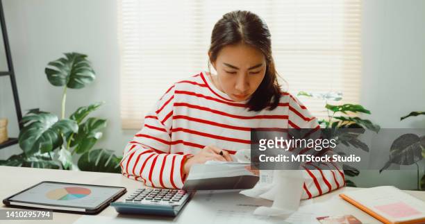 young asian woman with sweater sit in front of desk with tablet calculator focus on utility bills calculate check credit card receipt monthly expense bill at house. - manage invest stock pictures, royalty-free photos & images
