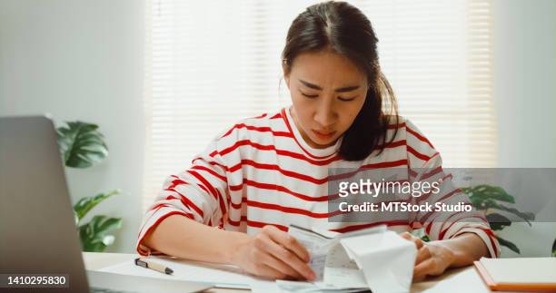 young asian woman with sweater sit in front of desk with laptop check receipt monthly expense bill feeling unhappy stress use calculator to calculate debt problem at house. - counting money woman stock pictures, royalty-free photos & images