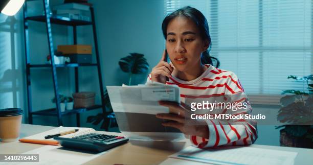 young asian woman housewife with sweater sit in front of desk check receipt monthly expense bill feeling unhappy stressed about debt problem fight with husband on phone in home at night. - tenant imagens e fotografias de stock