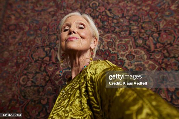 elderly woman against wall hanging rug - womens fashion stockfoto's en -beelden