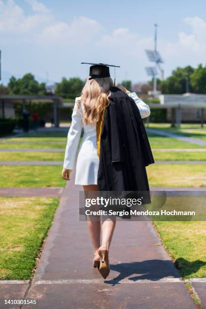 young blonde latino woman graduating from college, wearing a graduation cap and gown and walking away from the camera towards her future - walking away from camera ストックフォトと画像