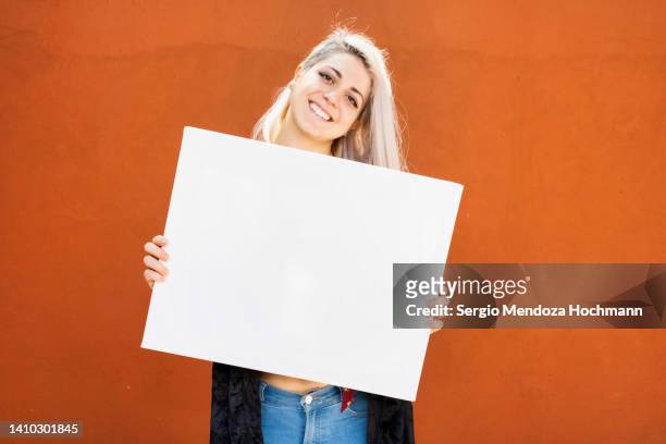 young latino woman smiling and holding a blank sign, with platinum blonde hair - person holding blank sign fotografías e imágenes de stock