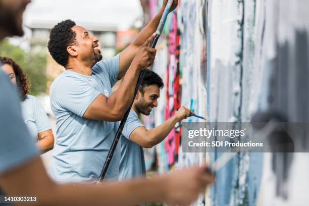 compañeros de trabajo sonriendo mientras pintan - comunidad fotografías e imágenes de stock