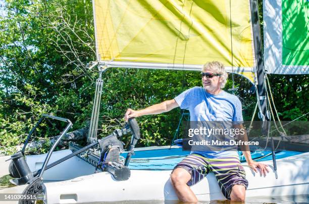 homme d’âge mûr assis sur la quille d’un petit catamaran - catamaran race photos et images de collection