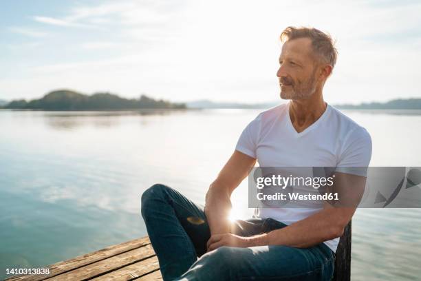 smiling mature man sitting by lake on sunny day - man front view stock pictures, royalty-free photos & images