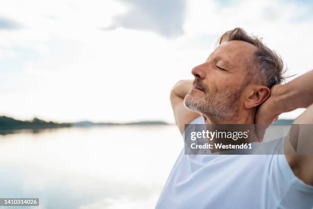 mature man relaxing with eyes closed at lake - hora del día fotografías e imágenes de stock