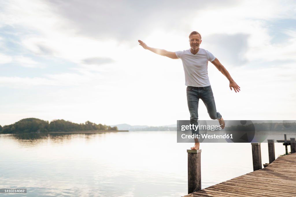 Happy mature man balancing on wooden post of pier
