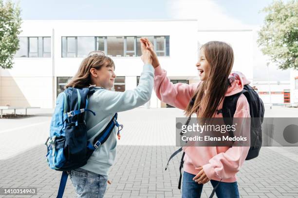 two teenage schoolgirls chatting, laughing in the school yard and high five each other. communication of adolescent schoolchildren with peers. - school boy girl stock-fotos und bilder