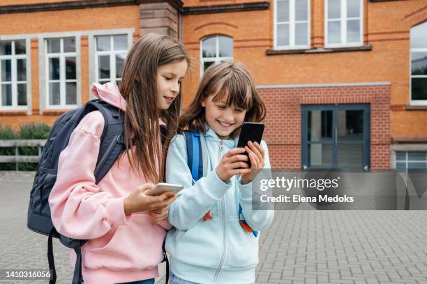 schoolgirl girlfriends in the school yard at recess watching videos and chatting with friends using a mobile phone - cell phones in school stock pictures, royalty-free photos & images