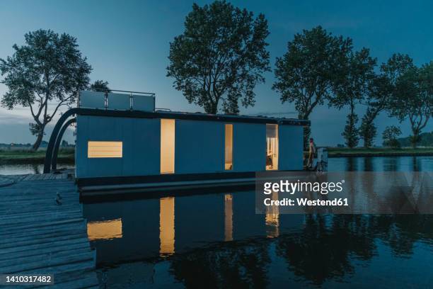 man standing on illuminated houseboat at sunset - hausboot stock-fotos und bilder