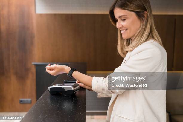 smiling businesswoman making contactless payment through smart watch at restaurant - watch payment stock pictures, royalty-free photos & images