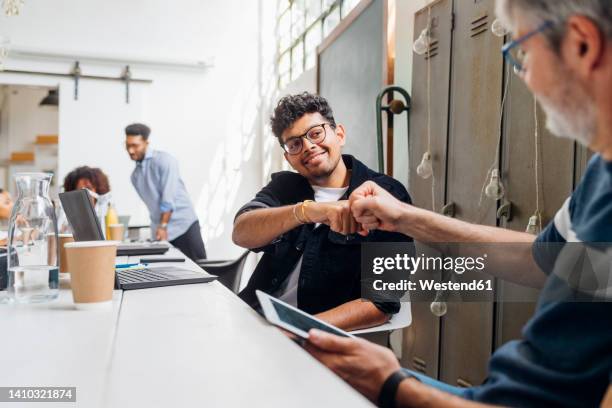 smiling businessman giving fist bump to colleague at workplace - fist bump photos et images de collection