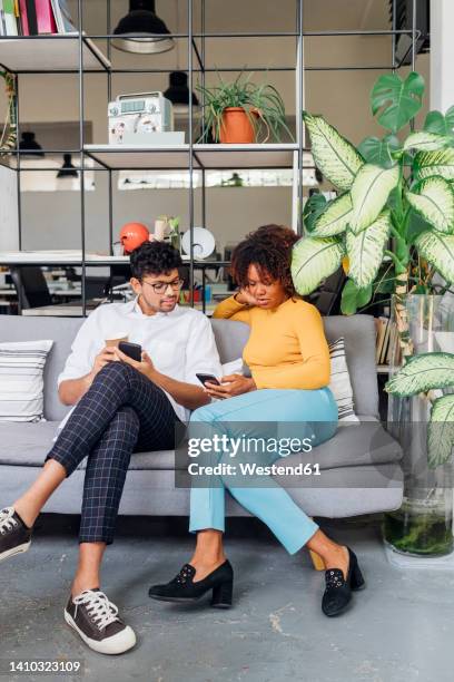 business colleagues using smart phone on sofa in office - legs crossed at knee stock pictures, royalty-free photos & images